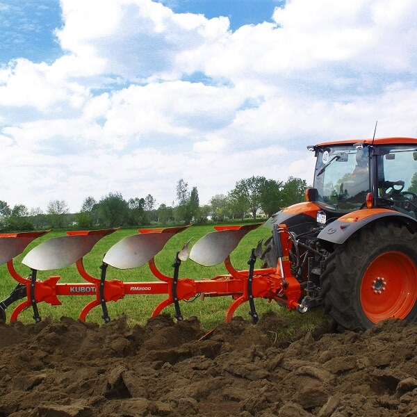 Un plan rapproché des mains d'un agriculteur tenant une poignée de terre riche et sombre dans un champ, avec un tracteur agricole Kubota orange flou en arrière-plan, illustrant pourquoi le choix de l'équipement agricole est déterminant au Québec.