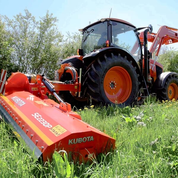 Un plan de trois-quarts avant d'un tracteur compact Kubota orange performant et propre, équipé d'un chargeur frontal, stationné à l'extérieur sur un terrain de gravier, illustrant une gamme complète d'équipements pour l'entretien de terrain.
