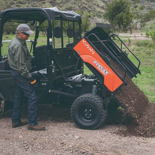 Un plan rapproché d'un outil agricole Kubota orange et robuste, spécifiquement une herse à disques ou un cultivateur de sol doté de disques métalliques tranchants, stationné sur un sol en gravier pour illustrer les outils agricoles essentiels pour maximiser la productivité.