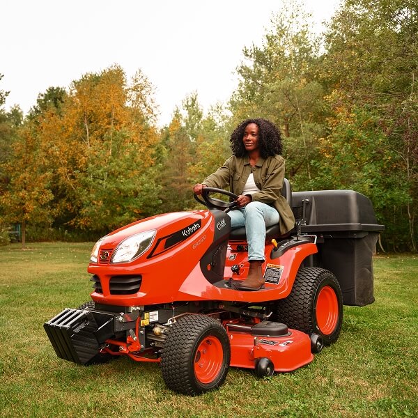 Une femme conduite un tondeuse à gazon rouge dans un jardin verdoyant.