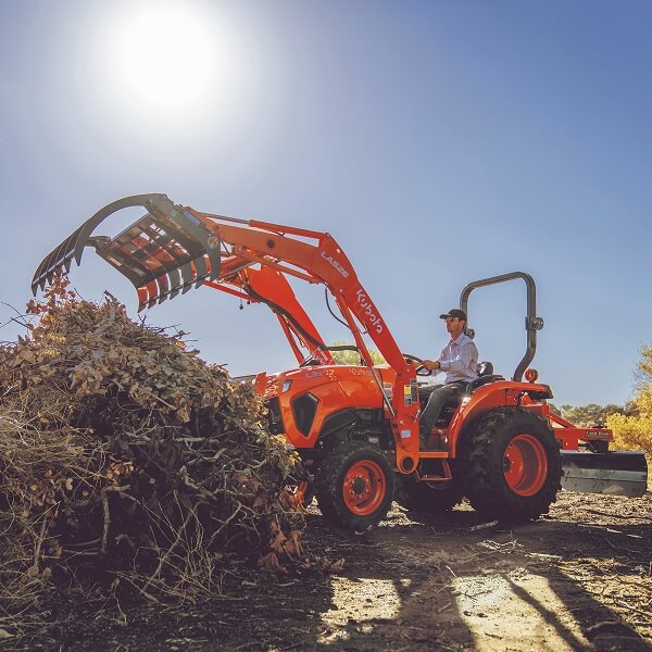 Un homme conduit un tracteur orange sur un champ de terre.